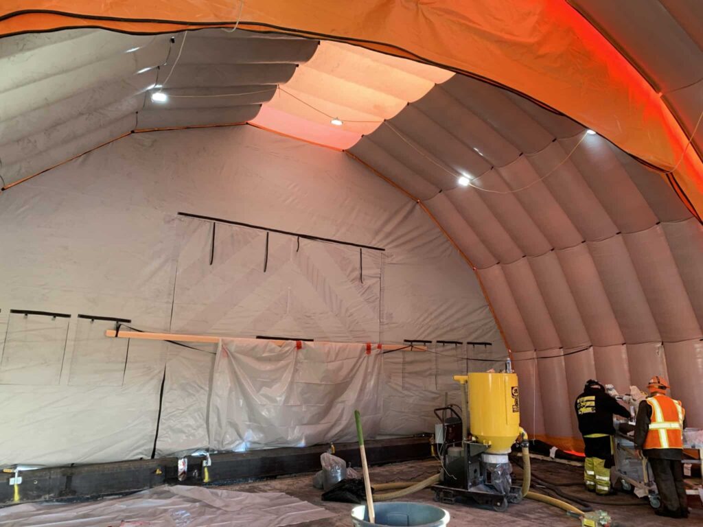 Contractors applying specialist roof coating inside the Njordair tent, lit by translucent roof panels